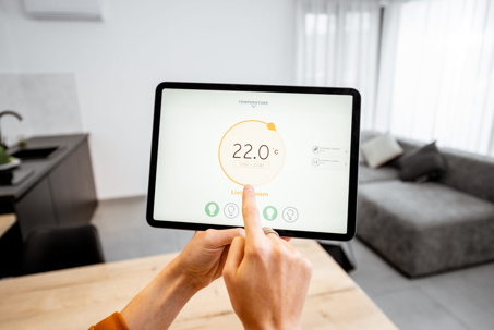 A person's hands adjust a smart thermostat on a tablet, displaying "22.0°C" in a modern home.