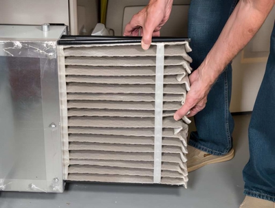 A person pulls a dirty, pleated furnace filter from an HVAC unit, illustrating filter replacement