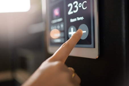 A person's hand adjusts a smart thermostat displaying "23°C Room Temp."