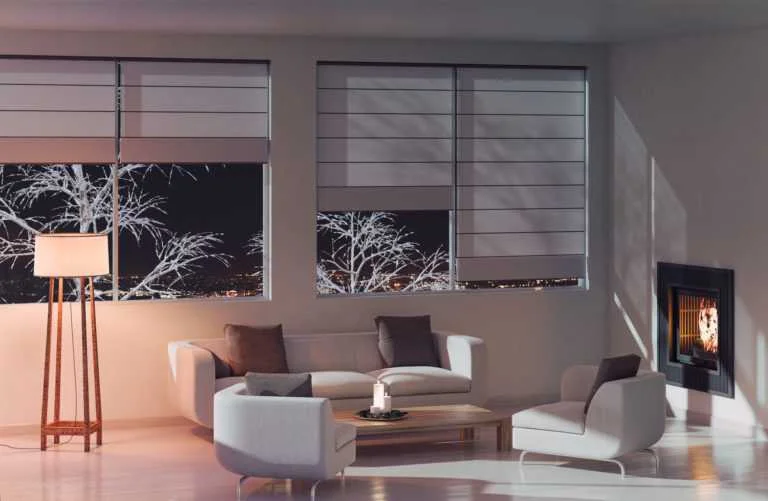 A serene living room at night with partially closed blinds, a fireplace, and soft lighting. White furniture and a wooden floor lamp create a comfortable and inviting home environment.